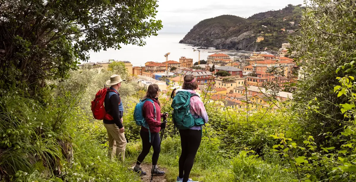 three hikers up a hill looking at view of houses by the coast